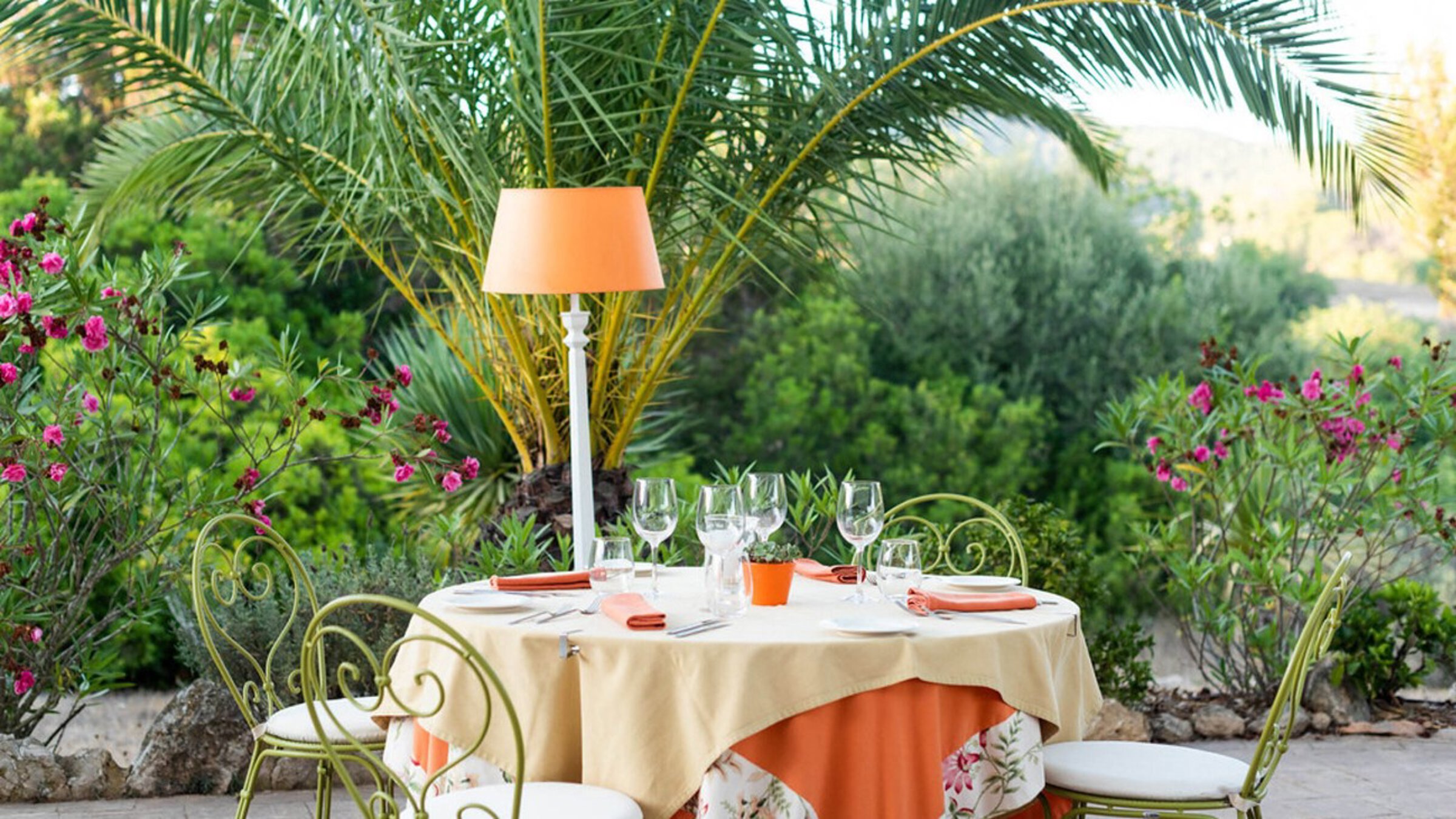 Round Table With Chairs, Lamp In A Green Garden With Palms